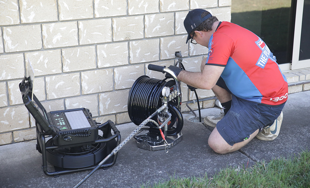 Plumber using a drain machine outside a home